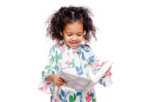 Pequeña chica afroamericana bastante de moda en vestido floral blanco mirando el cuaderno — Foto de Stock