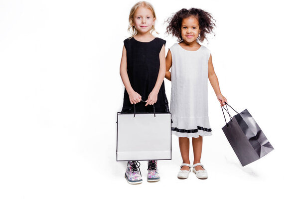 Little fashionable girls girlfriends of two different nationalities posing on a white background with shopping bags