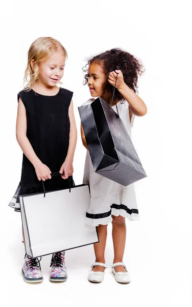 Chicas poco de moda de dos nacionalidades diferentes están posando sobre un fondo blanco con bolsas de la tienda. Una chica le muestra al otro lo que hay en su bolso. —  Fotos de Stock