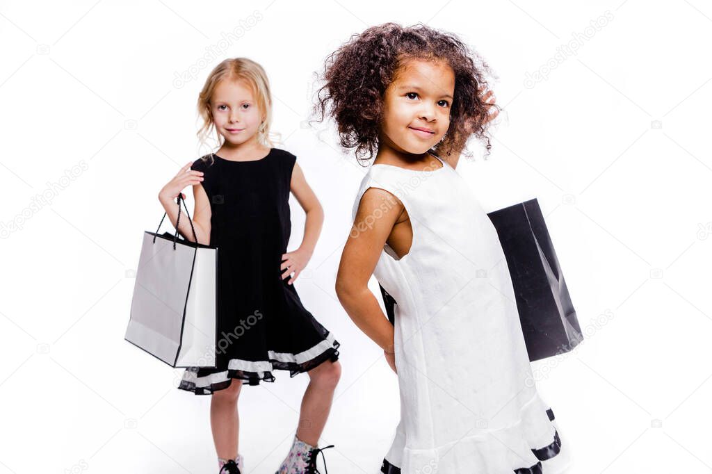 Little fashionable girls girlfriends of two different nationalities posing on a white background with shopping bags.