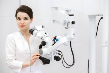 Beyaz önlüklü güzel ve ciddi bir dişçi elinde tıbbi malzemeyle kameraya bakıyor. Yatay fotoğraf