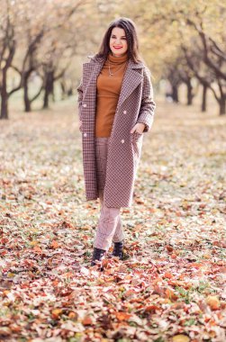 Sonbahar montlu, pantolonlu ve balıkçı yakalı güzel esmer kadın sonbahar parkında poz veriyor. Dikey fotoğraf