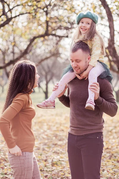 Anne, baba ve küçük kızları sonbahar parkında yürüyorlar. Aile birlikte zaman geçirir, rahatlar, iletişim kurar. Dikey fotoğraf