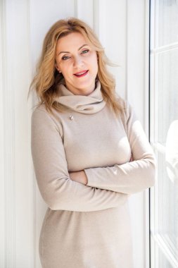 Zarif elbiseli güzel bir iş kadını güneş ışığında pencerenin yanında duruyor. Dikey fotoğraf