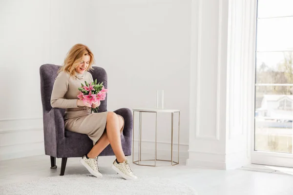 Beautiful Woman Tight Dress Sneakers Sits Chair Bouquet Flowers Smiles — Stock Photo, Image