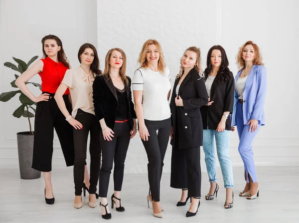 A group of women dressed in business style are standing together and posing at the camera. Horizontal photo