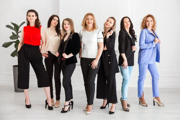 A group of women dressed in business style are standing together and posing at the camera. Horizontal photo