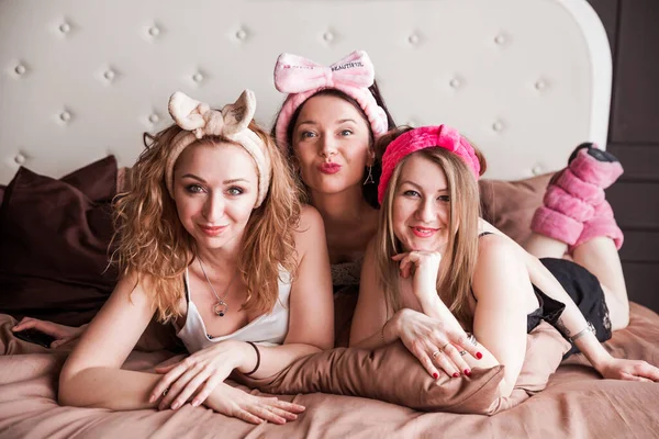 Three girls of a friend threw a pajama party on a plush bed. Girls smile and look at the camera. Horizontal photo