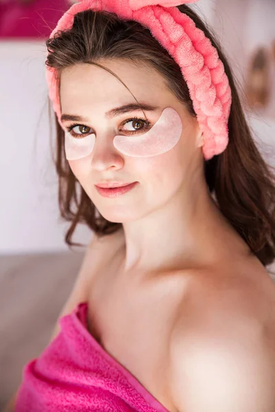 Beautiful woman is wearing pink headband in the morning and put patches under my eyes as a home care. Vertical photo