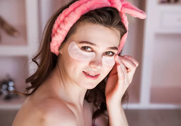 Beautiful woman is wearing pink headband in the morning and put patches under my eyes as a home care. Horizontal photo