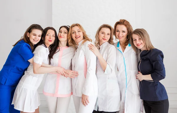 漂亮的年轻女医生身穿白衣 站在一面白墙的后面 女性拥抱是团队团结的标志 横向照片 — 图库照片