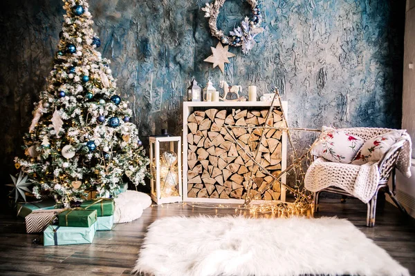 Living room decorated in New Year\'s style. The room has a Christmas tree with gifts, an armchair, a fireplace with wood and a white fluffy rug. Horizontal photo