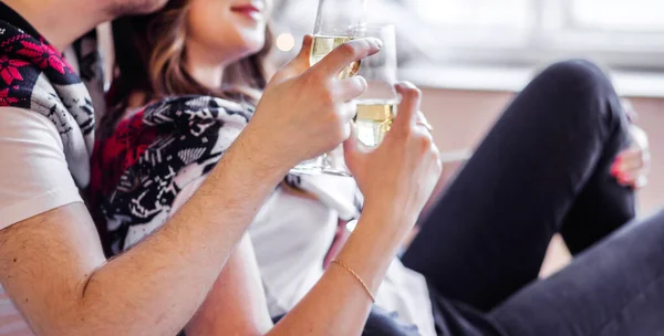 Man and woman in white t-shirts and knitted sweaters hold glasses of champagne in their hands. Horizontal photo