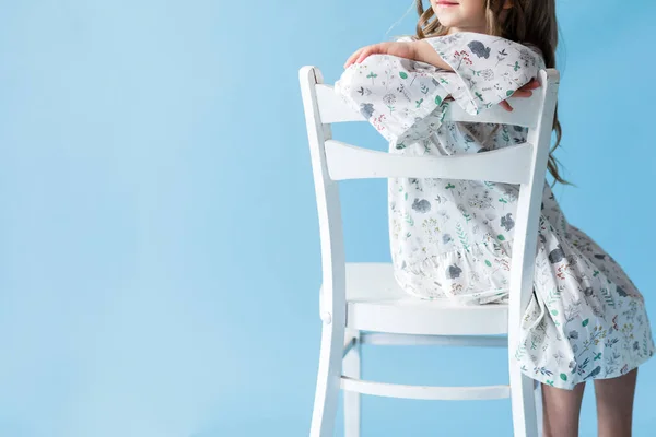Mała Dziewczynka Białej Sukience Siedzi Białym Krześle Niebieskim Tle Przestrzeń — Zdjęcie stockowe