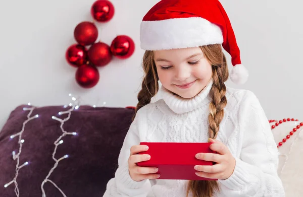 Una Niña Suéter Blanco Sombrero Santa Claus Mira Regalo Una —  Fotos de Stock