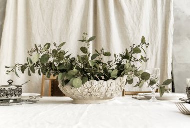 Süslü boho masası. Masa, üzerinde zarif tabaklar ve bardaklar olan bir masa örtüsüyle kaplıdır, üzerinde yeşil bir bitki bulunan bir vazo. Yatay fotoğraf