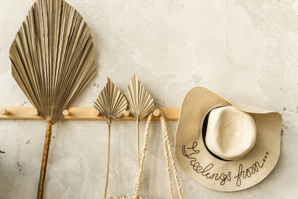 Fan leaf and straw hat hang on wooden hanger against gray wall. Horizontal photo