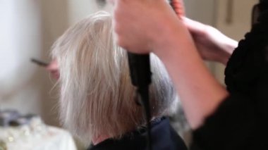 Kısa gri saçlı yaşlı kadın güzellik salonunda stil yapıyor. Video