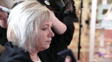 Kısa gri saçlı yaşlı bir kadın güzellik salonunda stil yapıyor. Oturan ve telefonda konuşan bir kadın. Video