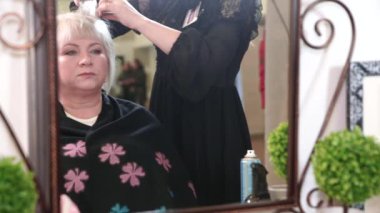 Kısa gri saçlı yaşlı bir kadın güzellik salonunda stil yapıyor. Aynanın karşısında oturan bir kadın. Video