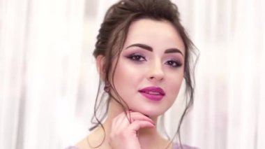 Güzel makyajlı, saç stili ve mor elbiseli esmer kız kameranın önünde poz veriyor.
