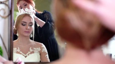 Güzel, genç bir gelin, şık bir saç stili, kafasında bir diyabet, küpeler ve beyaz bir elbise kuaförün koltuğunda oturuyor. Kuaför saçını düzeltir.