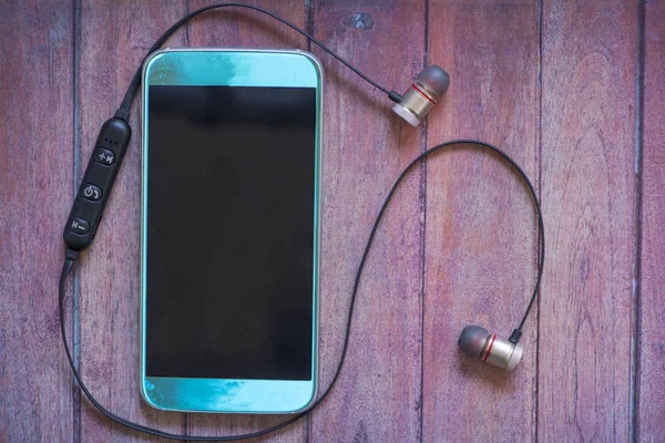 ダークブラウンの木製の Bluetooth ヘッドフォンで青い携帯電話 — ストック写真
