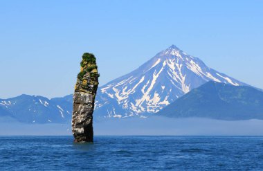 Rock in the sea against the background of the Viluchinsky volcano, Kamchatka, Russia. clipart