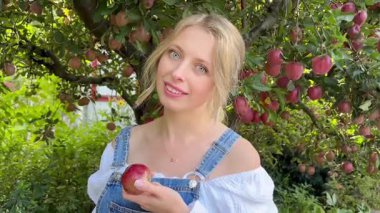 Elma tutan bir kadın. Bahçedeki Kadın. Elma bahçesinde meyve tutan ve gülümseyen bir kadın. Yüksek kaliteli FullHD görüntüler