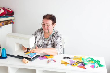Meslek, iş, patchwork kavramı. İşte gözlük yeşil string ile sıkı bir kadın, o ihtiyacınız olan tüm araçları beyaz masa donanımlı oturup dikiş makinesi ile çalışıyor