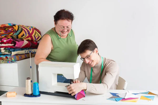 Empresa familiar, patchwork, conceito de ocupação. há casal coworking, um jovem que está aprendendo a costurar na máquina de costura e uma senhora idosa, sua avó, ela é uma costureira experiências — Fotografia de Stock