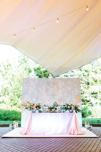 Arranjo, conceito de design. linda mesa de casamento para duas pessoas decoradas com grandes buquês de flores e velas em diferentes suportes localizados em uma tenda ao ar livre. espaço vazio para texto — Fotografia de Stock