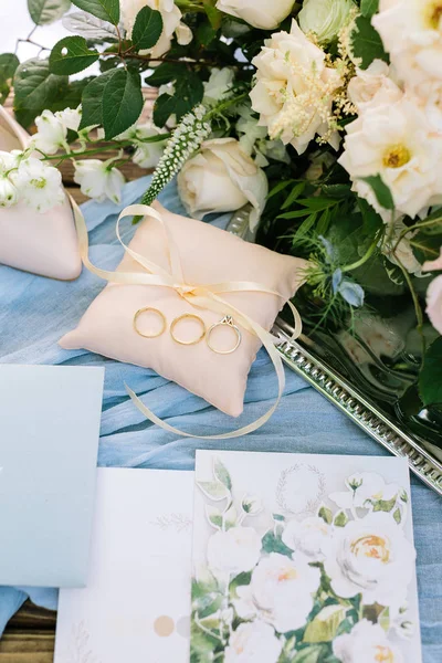 Present, surprise, wedding concept. nice top view of little peachy color pillow with thin ribbon, there is three golden rings on it, and nearby few postcards with painting of roses — Stock Photo, Image