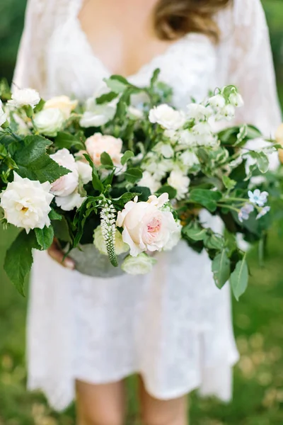 Tederheid, vrouwelijkheid, bruiloft concept. elegante en prachtige bruid in een zijde neglige met kant houden in haar delicate armen enorme en prachtige bos bloemen — Stockfoto