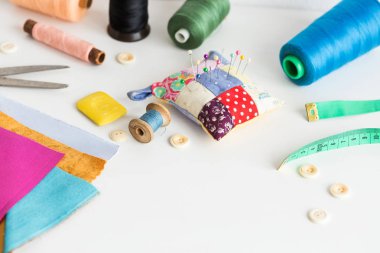 Dikiş araçları, yamalama, terzilik ve moda konsepti - beyaz bir masa üzerinde çalışma ortamı, iplik makaraları, düğmeler, metre, iğneleme, makas, renkli yama kumaş parçaları, sabun
