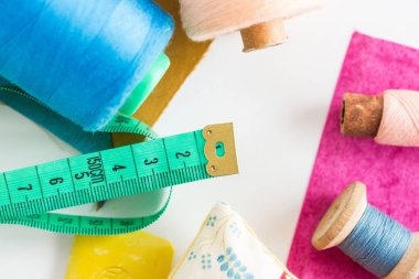 Dikiş, yama ve terzilik konsepti - ölçüm sayacına yakın çekim, bobinlerdeki mavi ve pembe iplikler ve beyaz arka planda mor ve hardal rengi yamalar, üst görünüm, düz yatış.