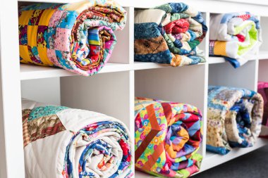 yama işi, dikiş ve moda konsepti - altı raflı beyaz kitaplık ve stüdyoda parlak tamamlanmış yorganlar, bitmiş ürünlerin deposu, yan görüş