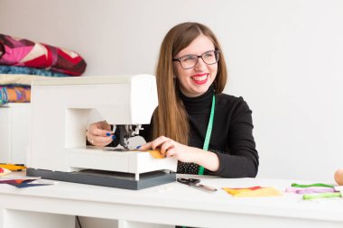 El işi, iş yeri, yaşam tarzı konsepti. Aydınlık renklerle süslenmiş dikiş ustasının çalışma odasında dikiş makinesi olan bir masa var, genç ve güzel kadın onunla çalışıyor.