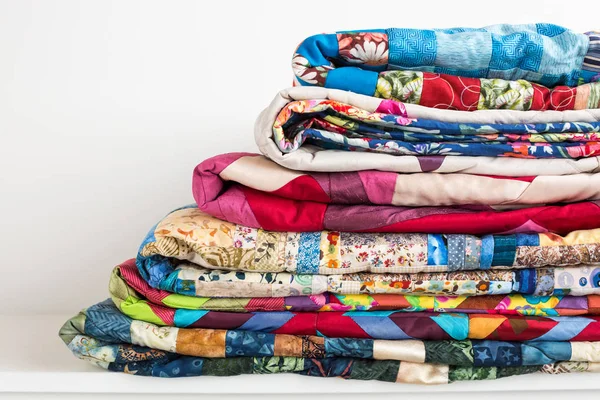 Dikiş, yama ve moda konsepti - güzel renkli yorganlar depolanmak için birkaç sıra yükseklikte katlandı ve depolandı, beyaz arka planda bitmiş tekstil dikişli ürünlerin satışı
