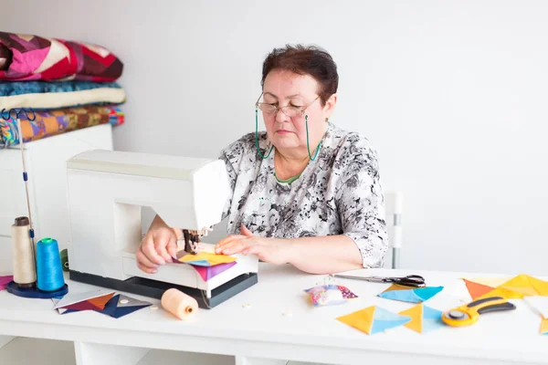 Ekipman, fabrika, tasarım konsepti. Çok ciddi ve katı bir kadın var. Renkli tonlarda farklı kumaş parçaları dikebilen dikiş makinesiyle işine konsantre oluyor.