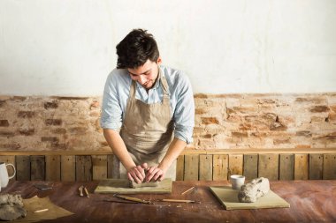 önlük ve kil masaüstü yoğurma forması giyen genç potter. Önden Görünüm. Sanat ve iş, hobi ve serbest çalışma kavramı.
