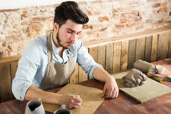 yakışıklı potter ware onun işyerinde kağıt üzerinde çizimler yapıyor. küçük işletme, el işi çalışmaları kavramı.