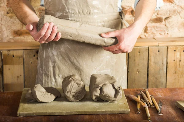 önlük ve kil, yönetim kurulu, kil ve araçları parçaları yalan çalışma tablosu üzerinde büyük bir parçası tutan forması giyen adam. Sanat ve hobi, çalışma kavramı.