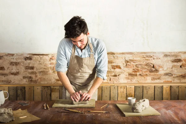önlük ve kil masaüstü yoğurma forması giyen genç potter. Önden Görünüm. Sanat ve iş, hobi ve serbest çalışma kavramı.