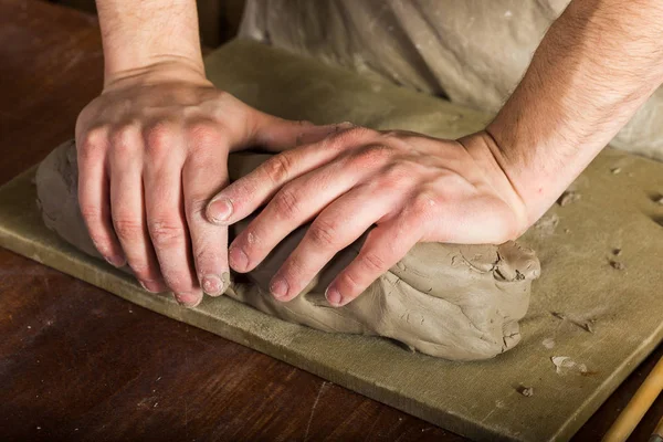 Handen met het grote stuk van aardewerk klei op te bord op bureaublad, close-up. Kunst en hobby en freelance werk concept. — Stockfoto