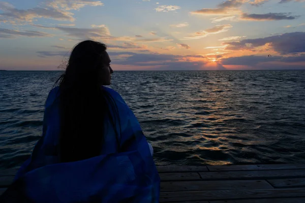 一个孤独而悲伤的年轻女人坐在海边的一座木桥上 看着夕阳 思想和专注 — 图库照片