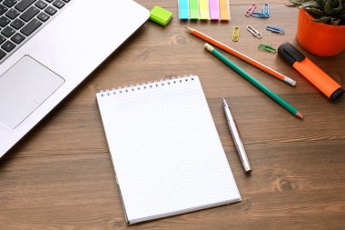 Notlar, kalemler, işaretçileri, kalem, kaktüs ile bir pot, bir dizüstü bilgisayar ve ahşap arka planda kağıt klipler için açık bir defter (ofis masası).