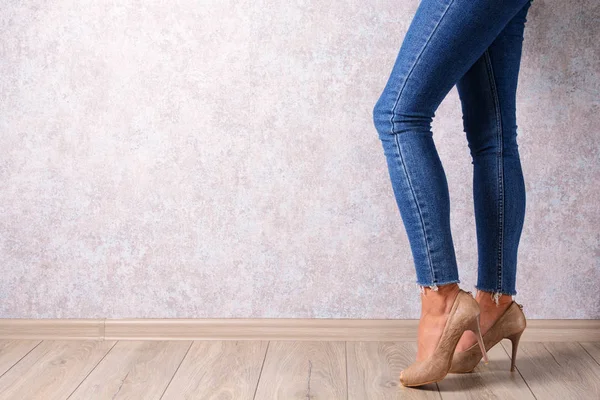 A young girl in high-heeled shoes and jeans on an abstract background. Youth, parties, fashion.