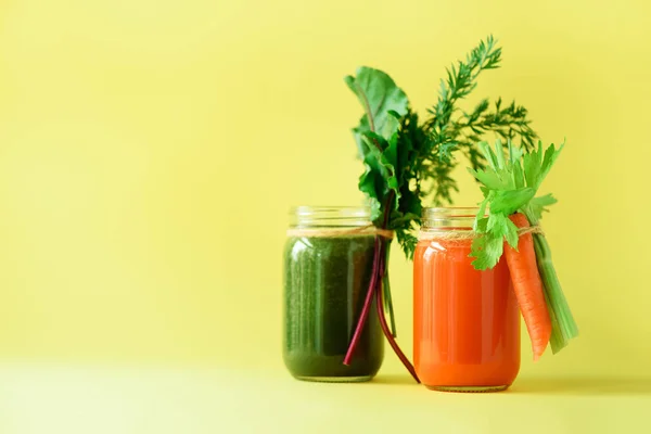 Gezonde biologische groene en oranje smoothies op gele achtergrond. Detox drankjes in glazen pot van groenten - wortel, BLEEKSELDERIJ, bieten Groenen en topjes. Kopieer ruimte. Zomer voedsel concept — Stockfoto