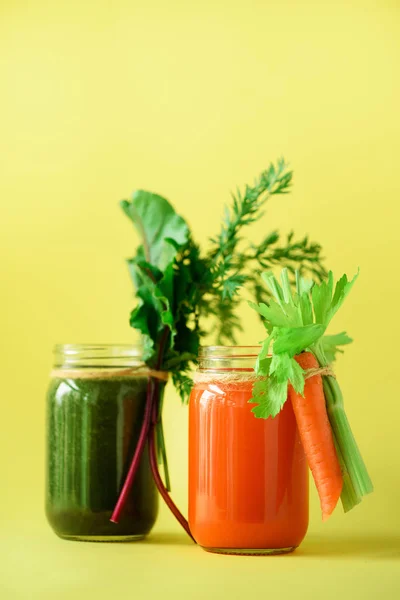 Здоровые органические зеленые и оранжевые коктейли на желтом фоне. Детоксикационные напитки в стеклянной банке из овощей - морковь, сельдерей, свекловичная зелень и топы. Принято. Концепция летней еды — стоковое фото
